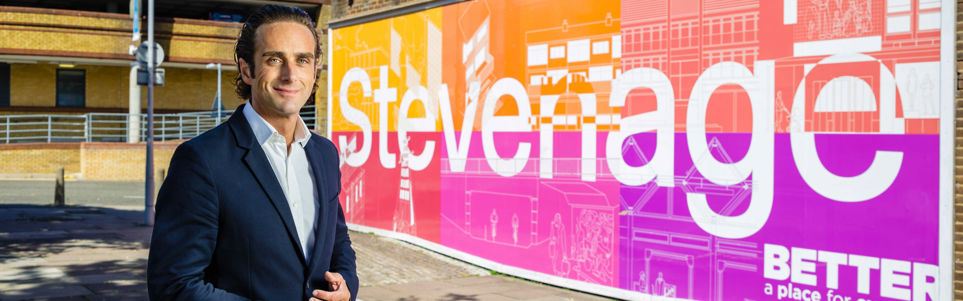 Alex Clarkson standing in front of the Stevenage sign in the town centre.