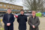 Bret, Alex and Adam facing the camera at the Oaks Cross shops. In the back ground is a tree, some recycling bins, parked cars and a low-rise block of flats.