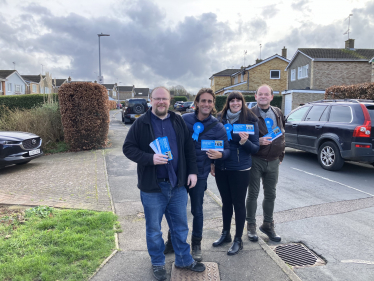 Alex Clarkson out campaigning with the Bandley Hill & Poplars Conservative team. In the background are houses, a road and a few parked cars.
